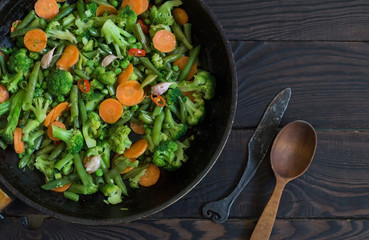 Fried vegetables in a frying pan on a dark wooden table