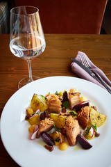 Baked potato slices and beets with vegetables and roast pork bacon on dark wooden table served in restaurant interior