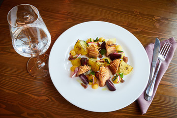 Baked potato slices and beets with vegetables and roast pork bacon on dark wooden table served in restaurant interior