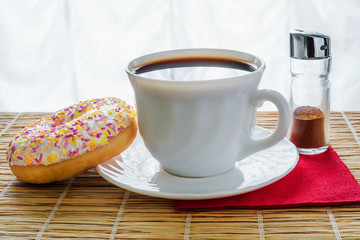 Still life with a cup of black coffee, donut and cinnamon on a mat