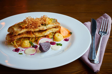 Baked cod fillet with vegetables in restaurant interior