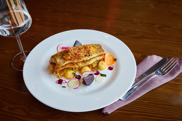 Baked cod fillet with vegetables in restaurant interior