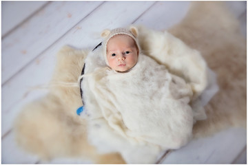 A small baby boy is having his first professional photoshoot. He is awake. He is covered with a white blanket.