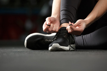 Cropped image of fitness lady tie laces in gym.