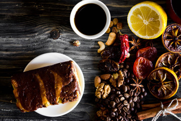 Dried slices of lemon, coffee beans, cinnamon, leaf tea, dried fruits and nuts on a wooden table. Cake on a white plate. Natural product.