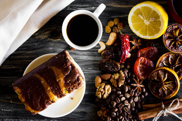Dried slices of lemon, coffee beans, cinnamon, leaf tea, dried fruits and nuts on a wooden table. Cake on a white plate. Natural product.