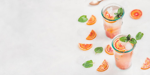 Blood orange fresh summer homemade lemonade with ice and mint in glasses, light grey marble background, selective focus, copy space