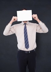 Business man holding card over face against navy chalkboard