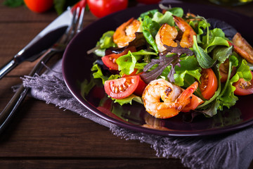 Fresh salad plate with shrimp, tomato and mixed greens (arugula, mesclun, mache) on wooden background close up. Healthy food. Clean eating.