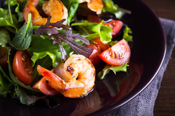 Fresh salad plate with shrimp, tomato and mixed greens (arugula, mesclun, mache) on wooden background close up. Healthy food. Clean eating.
