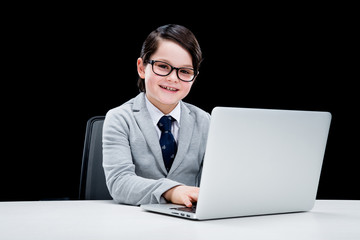 Little boy in formal suit and eyeglasses working with laptop and smiling