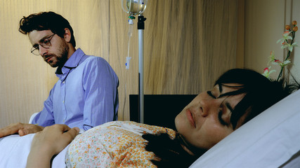Sick ill woman sleeping in hospital while husband is reading