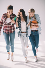 Three happy beautiful girls students with books walking together on white