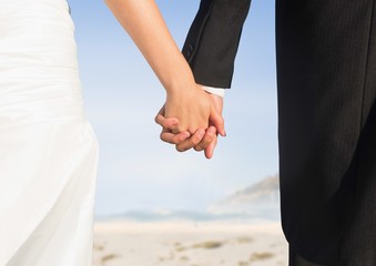 Bride and groom lower bodies holding hands against blurry beach
