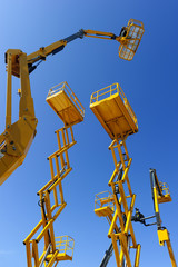 Scissor lift platform, cherry picker, aerial platform with bucket, articulating boom and other yellow construction cranes and machines, heavy industry, blue sky on background, bottom view 