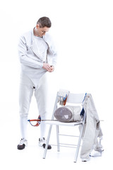 Young man professional fencer putting on protective costume on white