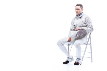 Young man professional fencer holding sword and mask while sitting on chair