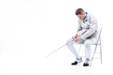 Young man professional fencer sitting on chair with helmet and sword