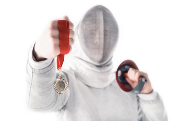 Portrait of professional fencer in fencing mask holding medal and rapier on white