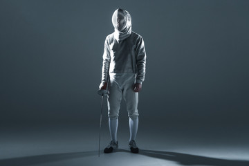 Fototapeta premium Professional fencer in fencing mask with rapier standing on grey