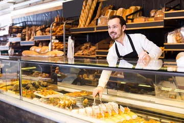  Male shop assistant demonstrating fresh delicious pastry in bakery © JackF