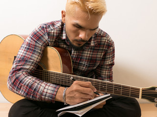 Young hipster composing the song with guitar .