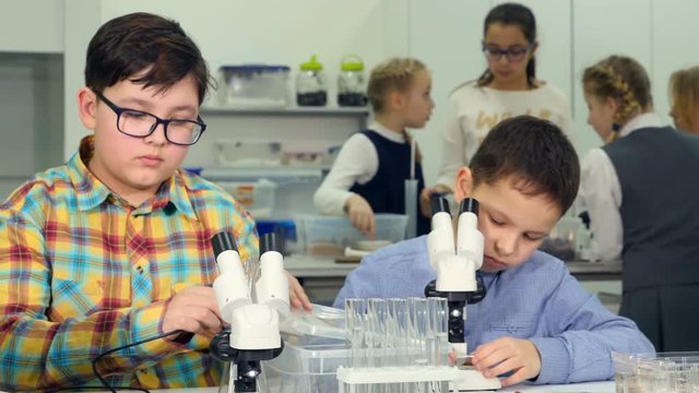 Children studing biology, chemistry in elementary school biology class. Looking into a microscope. 4K.