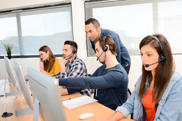 group of young people with desktop computer in row and headset training with teacher instructor in customer service call support helpline business center