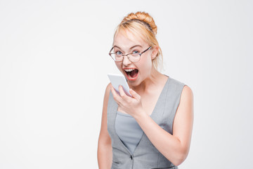 Angry young woman in glasses with mobile phone looks furious, enraged and mad. Irritated girl...