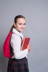 Obraz premium A schoolgirl in a uniform is standing with a book and a backpack
