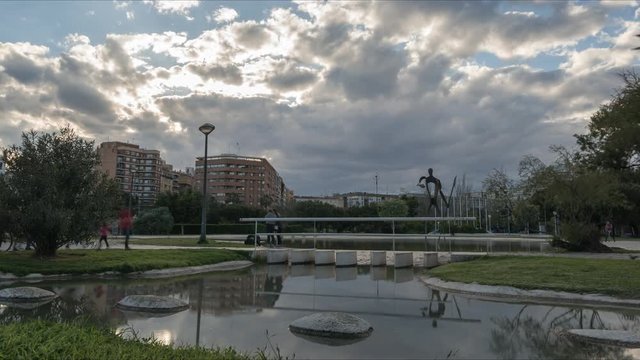 Valencia Turia Gardens Cloudy afternoon time-lapse sunset at the the old dry riverbed, water reflection, Spain Europe. Tourists and people walking and taking photos. Sun rays poke through the clouds