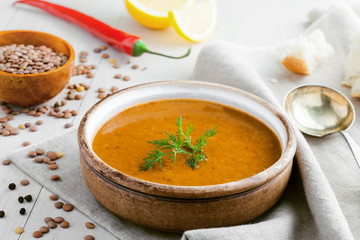 Soup made of lentil and vegetables in a rustic bowl  with bread on a canvas tablecloth. Delicious healthy vegetarian food on a white wooden table.