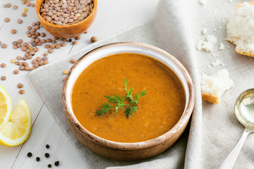 Delicious soup made of lentils in a rustic clay bowl served on a canvas tablecloth. Healthy vegetarian meal on a table. Top view shot.