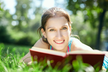 Beautiful girl lies on meadow and reads the book. Education and vacation concept