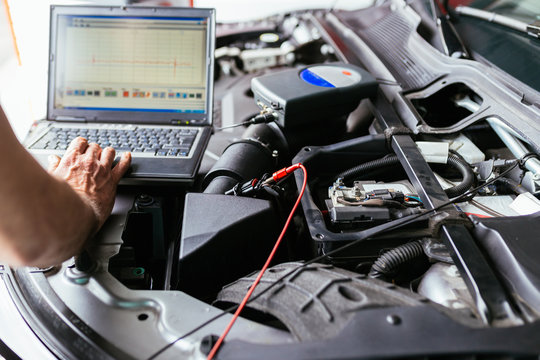 Auto mechanic repairing car and typing notes on laptop. Selective focus.