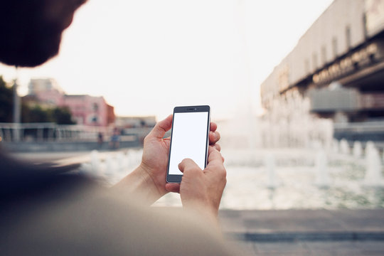 Phone With Blank Screen In Hands, Over The Shoulder View. Shot With Third-person View. Clipping Path For Screen.