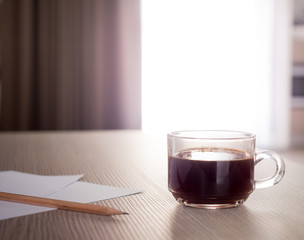 A cup of coffee and notebook on wood table . Coffee break in morning ,break working  / selective focus.Blank seating  indoor in living room .copy space for create idea for business.