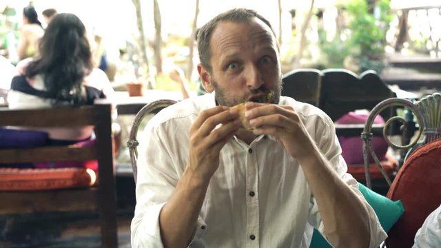 Funny, hungry man eating sandwich in cafe
