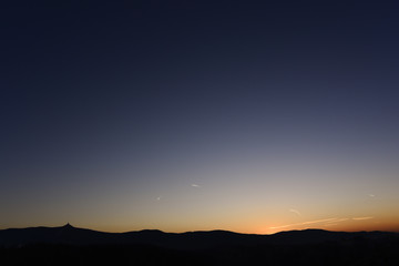 Clear blue sky during sundown behind silhouette of hills.