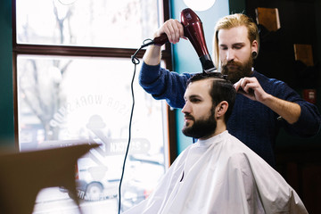 Barber uses a hair-dryer while sectioning man's hair