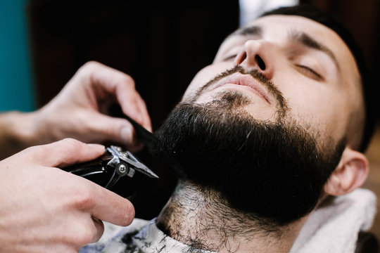 Barber shapes man's beard with a clipper