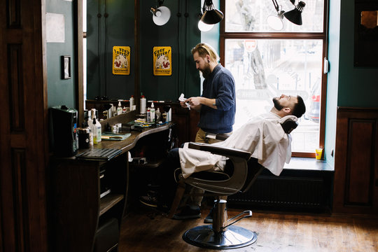 Blond barber cleans his clipper standing before the client