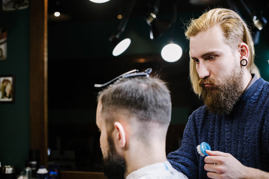 Bearded man sits straight while barder cuts his hair