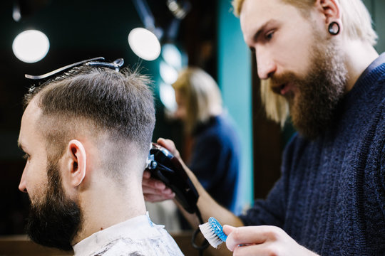 Blond bearded barder makes fade on man's hair attentively