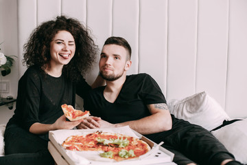 Obraz na płótnie Canvas Funny young couple eats pizza lying on bed