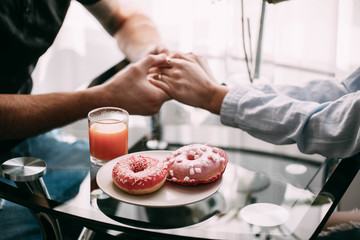 Plate with pink donuts stands by man and woman holding their hands together on the table