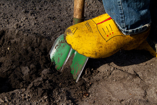 Digging the soil with a green spade, wearing clogs