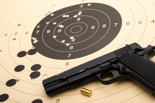 9 mm black pistol - handgun over paper target with hits - holes and empty cartridge shell