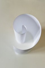 Paper spiral/Curved paper sheet looking like the number nine on a beige background.