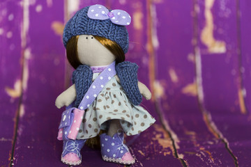 Текстильная кукла в голубой платье в горошек, в вязанных синих шапке и жилете, в кедах из фиолетового и розового фетра, с сумочкой из фетра  - obrazy, fototapety, plakaty
